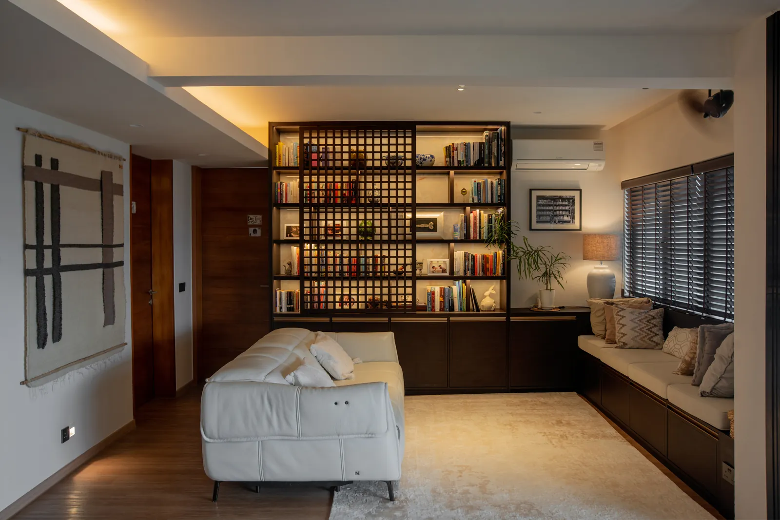 Villa in the Sky: living room with a white sofa, a window seat and lit bookshelves behind a timber lattice screen
