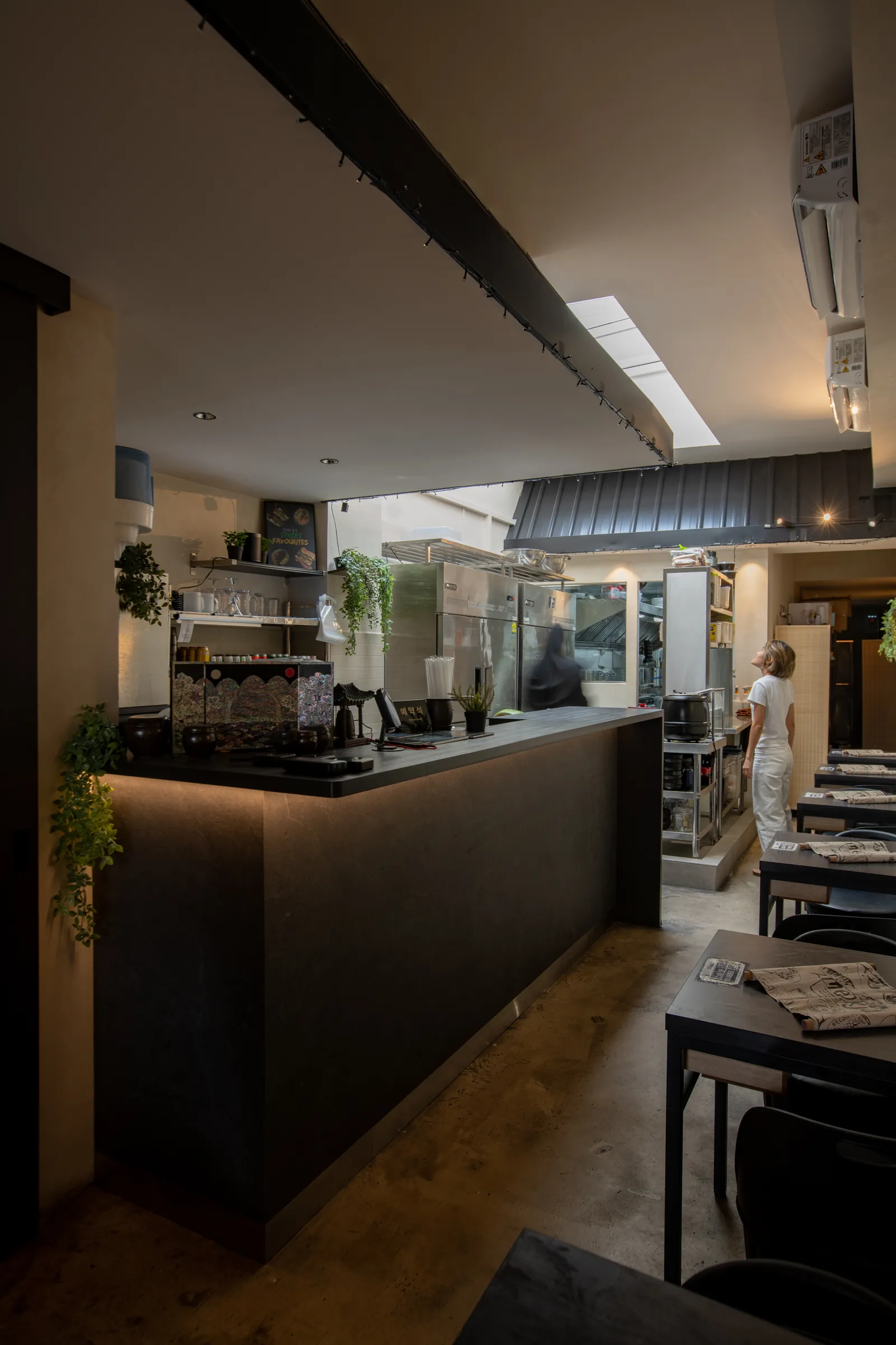 Hanok Shophouse: dark timber counter under the hanok-style roofline, with the open kitchen beyond