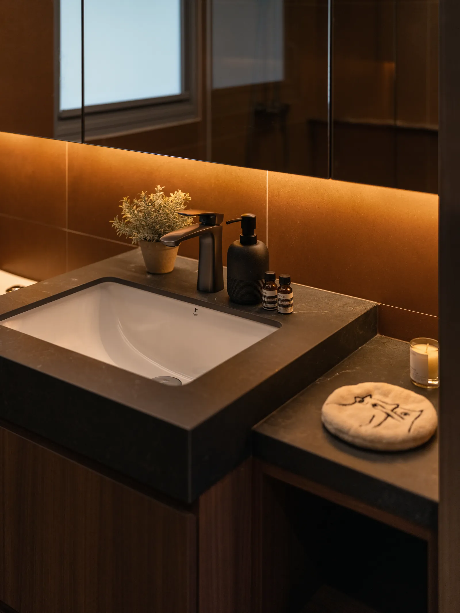 Mid Century Sanctuary: dark stone vanity with an undermount basin, lit from behind the mirror