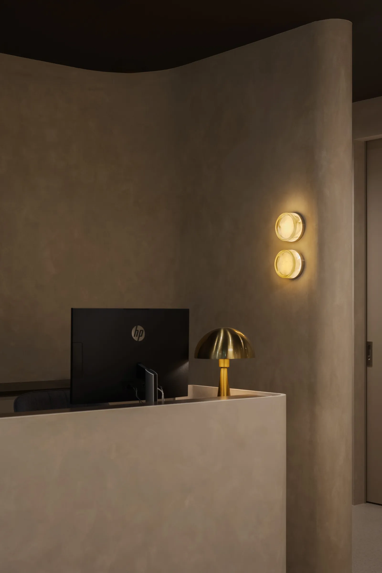 Rooms for Renewal: reception desk with a brass lamp and twin wall lights against textured plaster