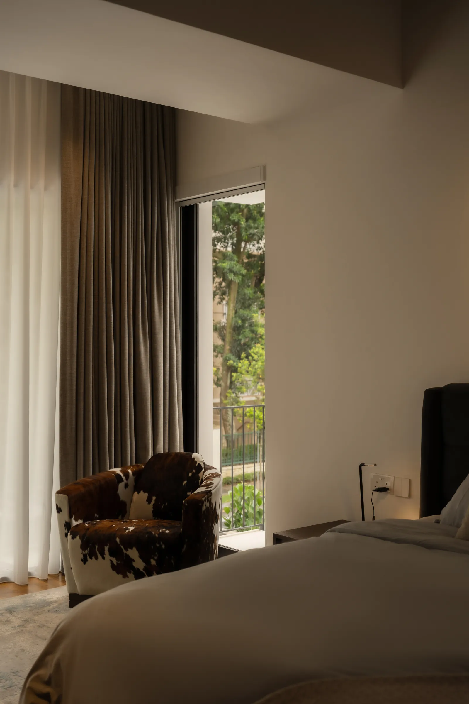 The Art of Retreat: bedroom corner with a cowhide armchair beside a window to the trees