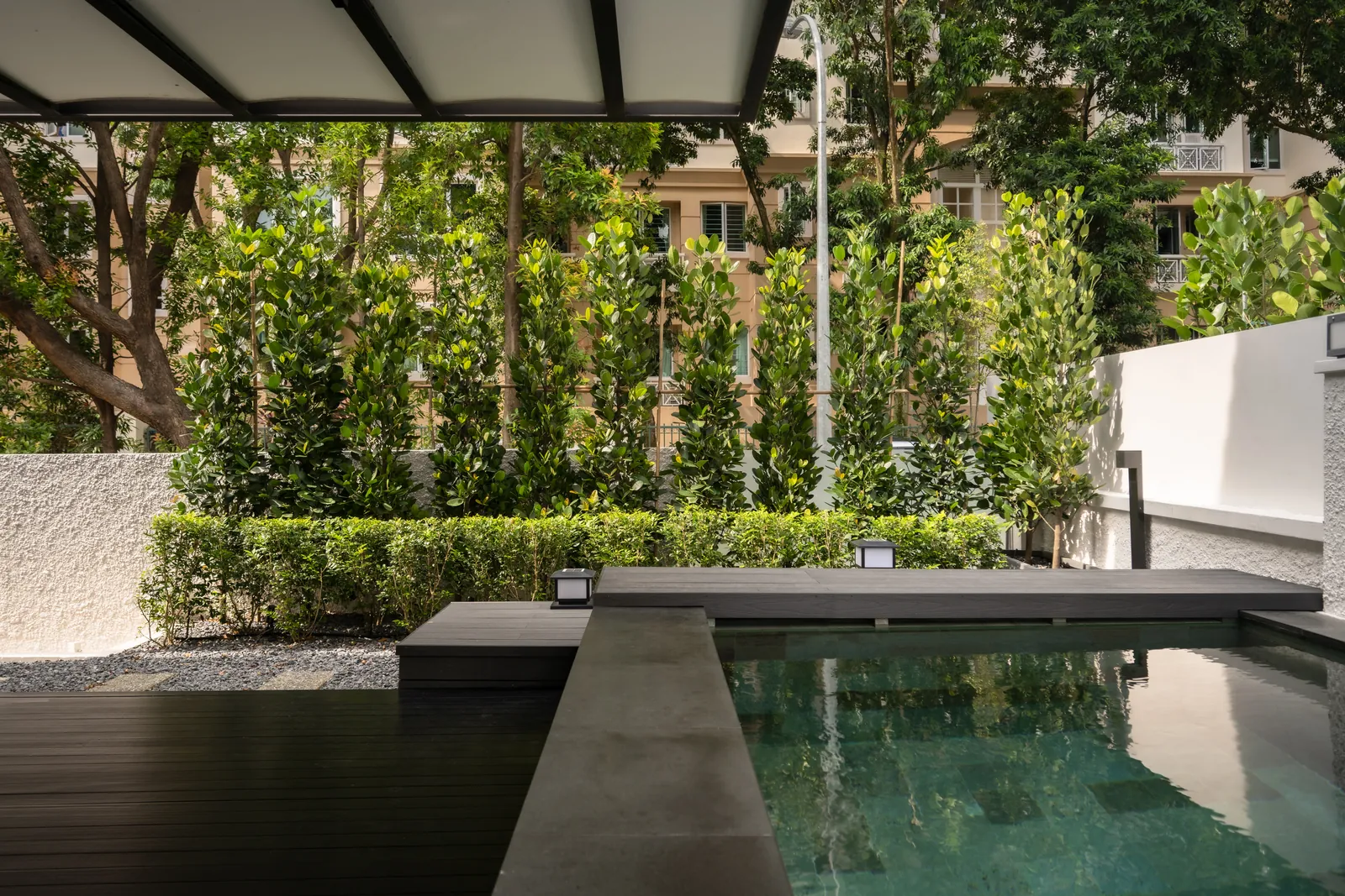 The Art of Retreat: pool terrace under a pergola, screened by a hedge and trees