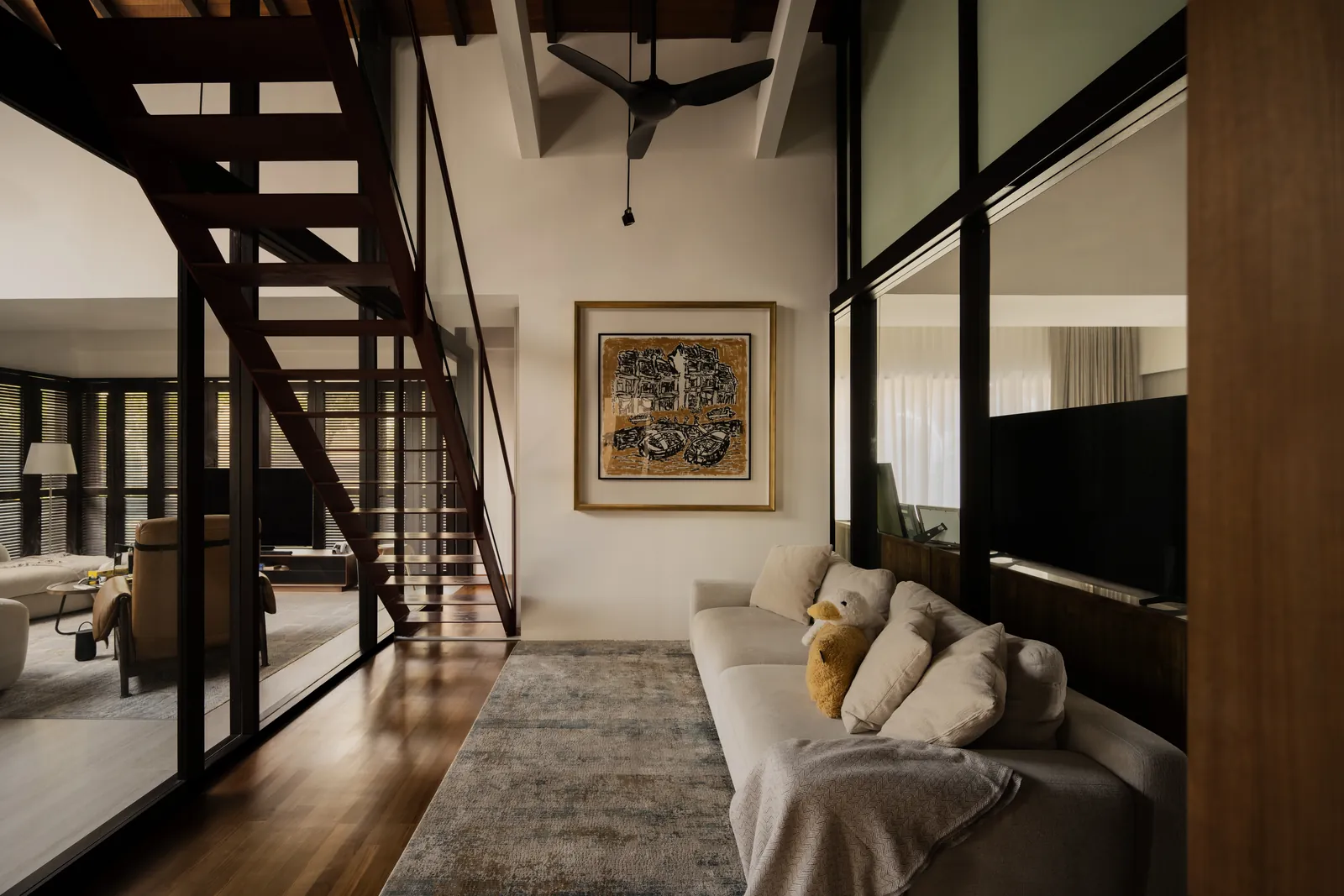 The Art of Retreat: lounge beneath the open steel stair, with a framed artwork and glass walls to the next room