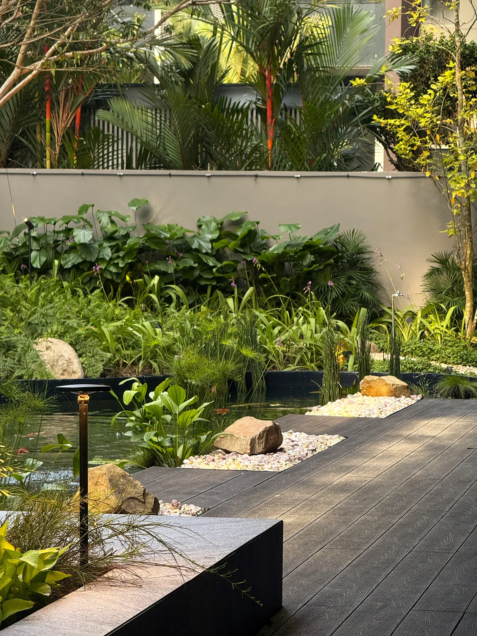 The Garden Within: timber deck beside the koi pond, with boulders, gravel and dense planting behind