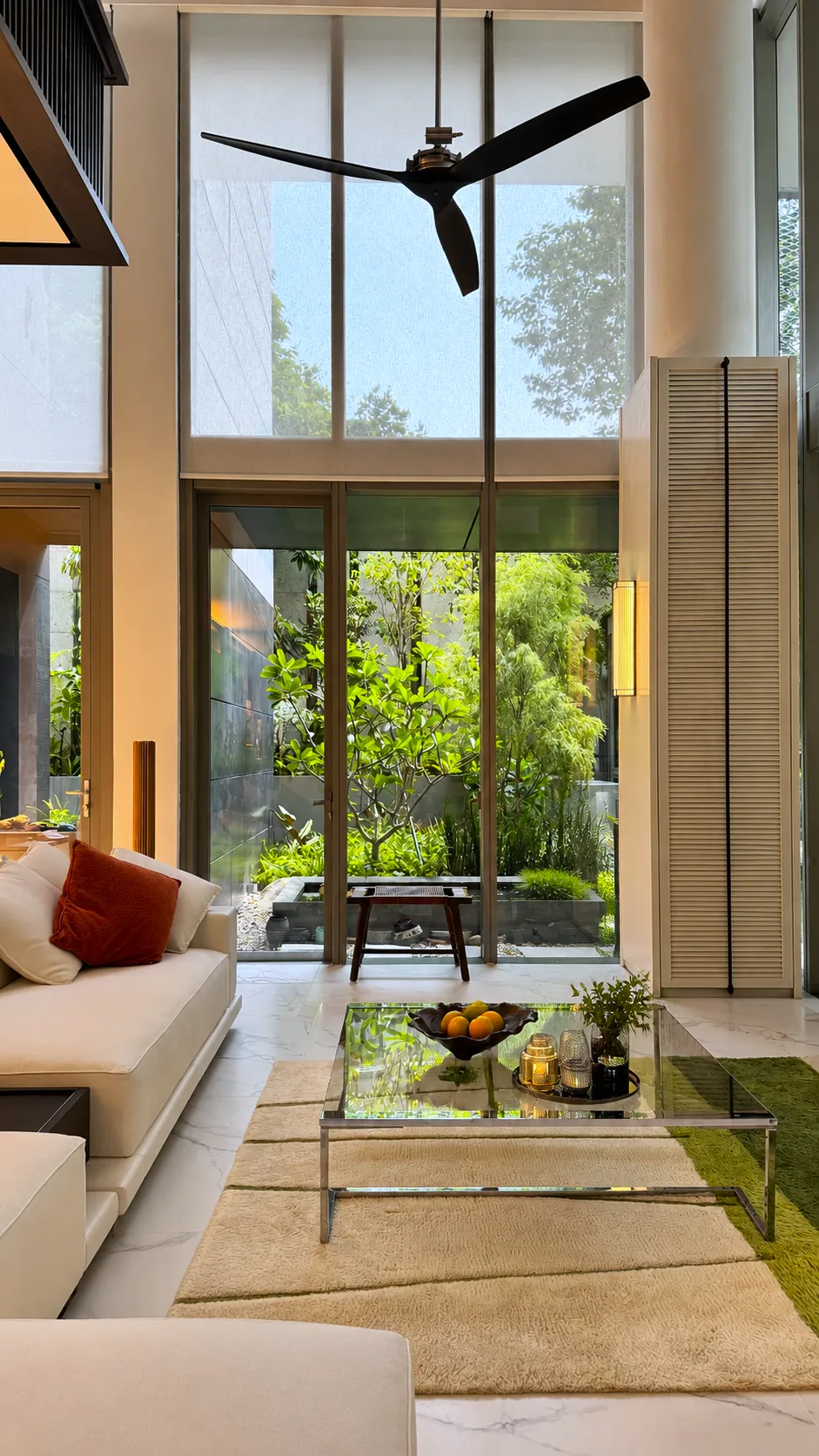 The Garden Within: double-height living room with a ceiling fan, opening onto a planted side garden