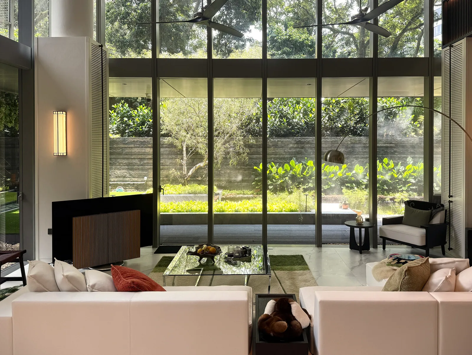 The Garden Within: living room with white sofas facing full-height glass onto the garden