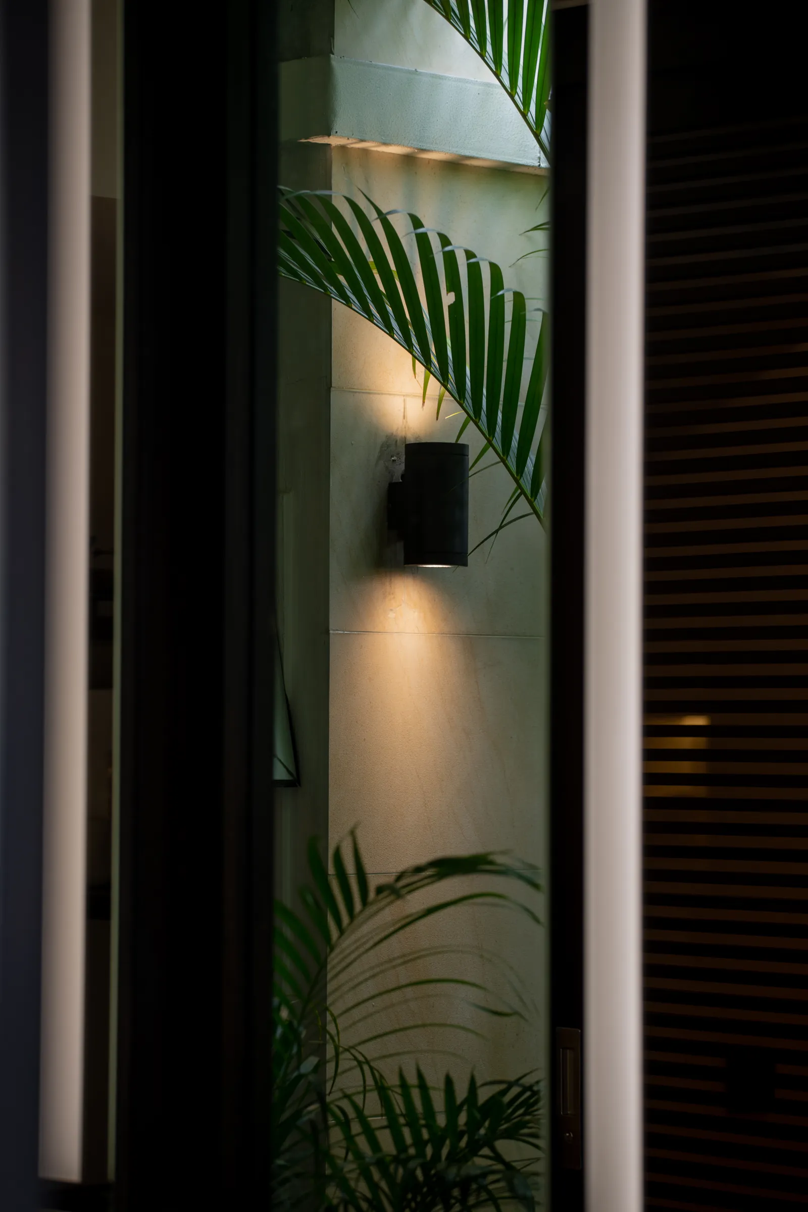Villa in the Sky: palm fronds and a wall light seen between lit mirror strips